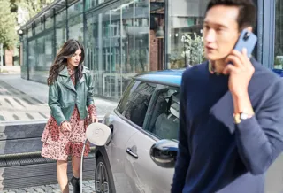 An image of woman charging a car while a man talks on the phone