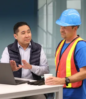 Man discussing something on his laptop with a man in a hard hat and high-vis top