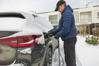 Man plugging in his EV to charge with snow on the ground