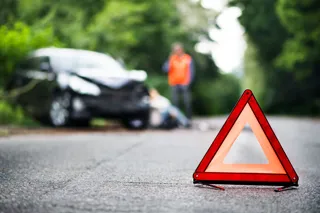 red accident triangle on a road with crashed vehicle in background