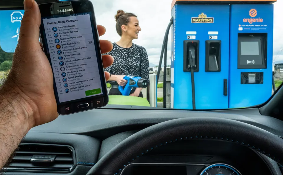 Person looking at phone while another plugs their electric car in